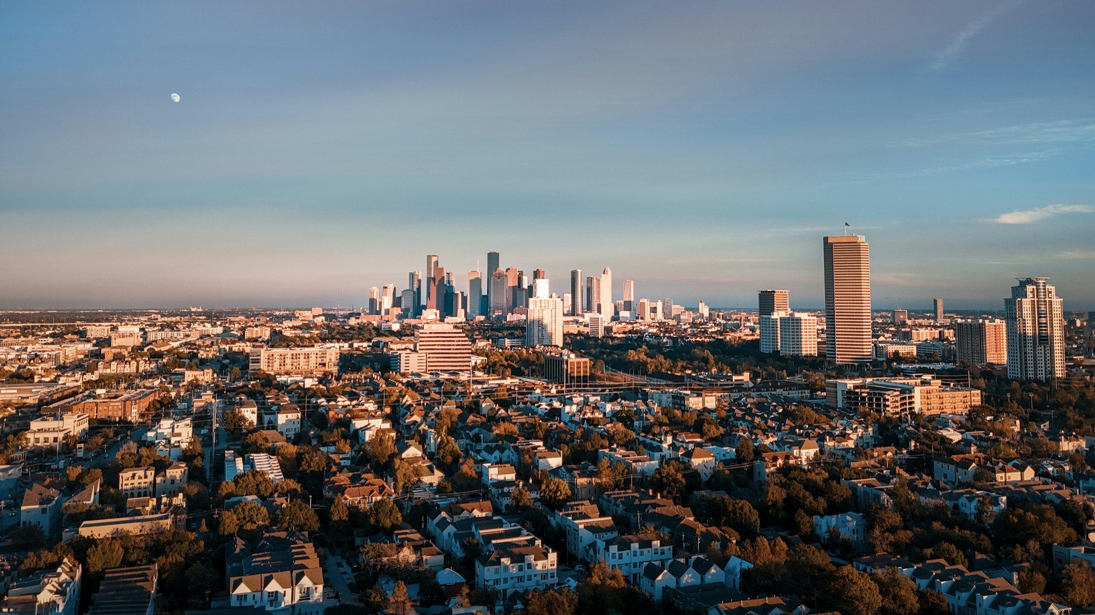 Aerial view of Houston at dusk, with neighborhoods in the foreground and the skyline on the horizon
